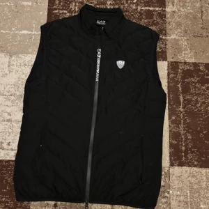 EA7 väst svart - Säljer västen nu för den blivit liten på mig den är som ny och kostar 245$ ny pris vilket är ca 2500kr.          Kolla in i deras hemsida: https://www.armani.com/en-us/ea7/premium-shield-packable-gilet-cod-8NPQ02-PNE1Z-1200/?vsFromReqId=01933fef152dfe9fbf4c211b8a44c2