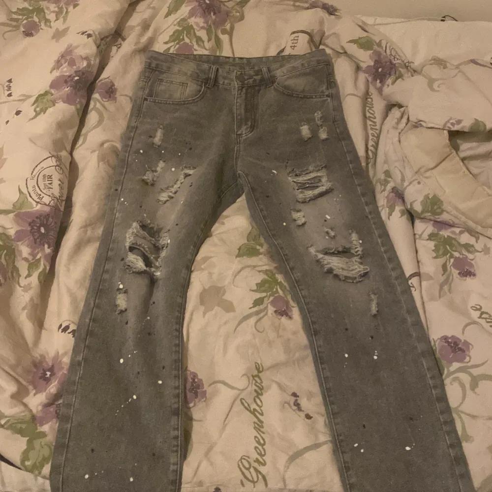 Säljer ett par grå jeans med coola slitningar och färgstänk. Jeansen har klassisk femficksdesign och är i bra skick. Perfekta för höst och vår! Jag har ingen aning vad märket är eftersom jag fick dem som en gåva. Jeansen är nya och har aldrig varit använda utomhus.. Jeans & Byxor.