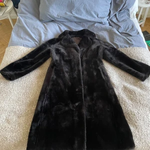 Brun pälsjacka från F. Greenfield & Sons - Säljer en elegant svart pälsjacka från F. Greenfield & Sons. Jackan är lång och har en klassisk stil med långa ärmar och en mjuk, lyxig känsla. Perfekt för kalla vinterdagar och ger en sofistikerad look. Tillverkad i England med hög kvalitet. Drar ner priset lite för att den saknar en knapp. 