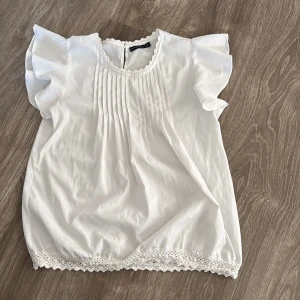 Vit blus med spetsdetaljer - Säljer en superfin vit blus  med volangärmar och spetsdetaljer vid hals och nederkant. 