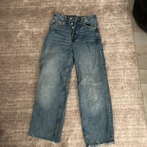 Blå jeans från H&M Divided - Säljer ett par snygga blå jeans från H&M Divided i storlek XS. De har en hög midja och en loose passform med fransiga kanter längst ner. Perfekta för en avslappnad stil och passar till alla tillfällen. Säljer för att dem är för små