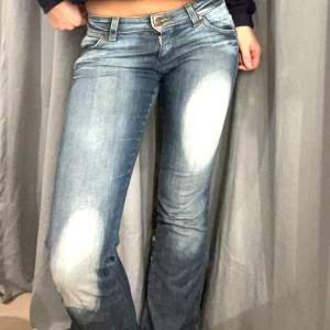 Säljer ett par snygga blå jeans i bootcut-stil. De är lågmidjade och har en klassisk femficksdesign med slitningar på låren för en trendig look. Perfekta för både vardag och fest!