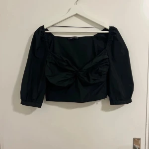 Svart topp från Zara Woman - Säljer en snygg svart topp från Zara Woman i storlek S. Toppen har en offshoulder-design med puffiga trekvartsärmar och en knytning framtill som ger en fin detalj. Perfekt för festliga tillfällen!