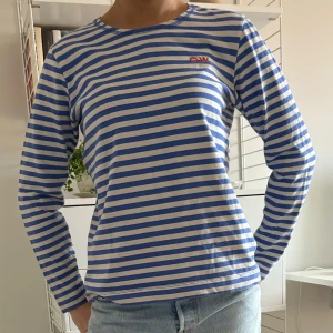 Randig långärmad tröja  - Säljer en superfin randig tröja från Carin Wester i blått och vitt. Den har långa ärmar och en liten röd logga på bröstet. Perfekt för både vår och höst, och den är gjord i mjuk bomull. Passar perfekt till jeans eller kostymbyxor!