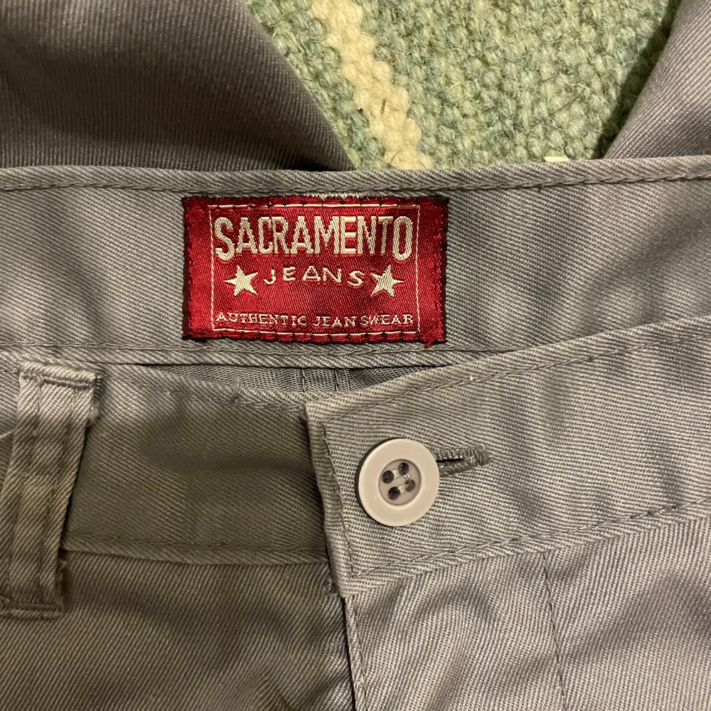 Säljer ett par grå byxor från Sacramento Jeans. De har en rak passform och är midwaist med knappar framtill. Perfekta för en avslappnad stil eller vardagsbruk. Passar bra till både t-shirt och skjorta.. Farkut & Housut.