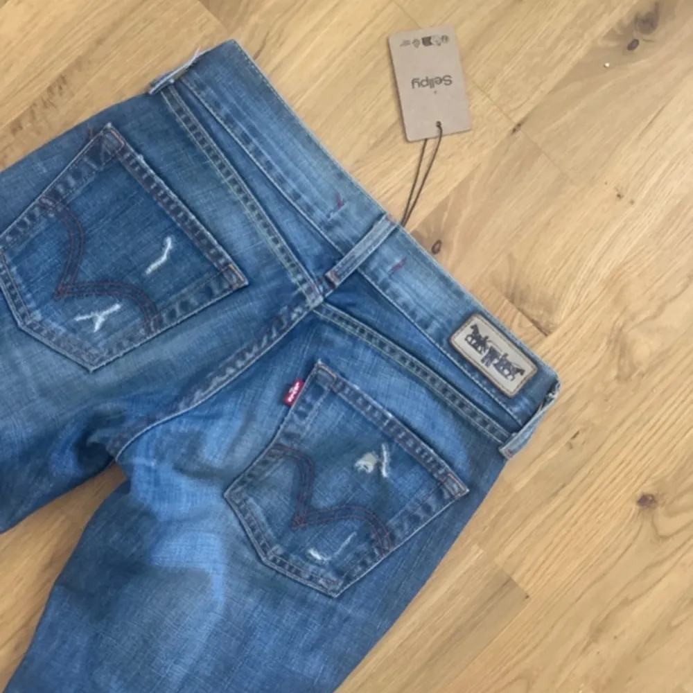 Säljer ett par snygga blå lågmidjade jeans från Levi's. De är i en klassisk straight fit och har en cool, sliten look med några små revor. Märket är Levi's, vilket garanterar bra kvalitet och hållbarhet. Passar perfekt till vardags!. Jeans & Byxor.