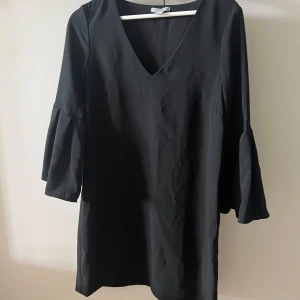 Svart klänning med v-ringning - Säljer en elegant svart klänning med v-ringning och trekvartsärm. Klänningen har en lös passform och är perfekt för både vardag och fest. Materialet känns mjukt och bekvämt mot huden. Passar bra till höst och vinter.