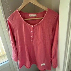 Rosa långärmad topp från Odd Molly - Säljer en superfin rosa långärmad topp från Odd Molly. Den har en söt spetsdetalj runt halsringningen och knappar framtill. Perfekt för en avslappnad vardagslook eller att klä upp med accessoarer. Toppen är i bra skick och redo för en ny ägare!