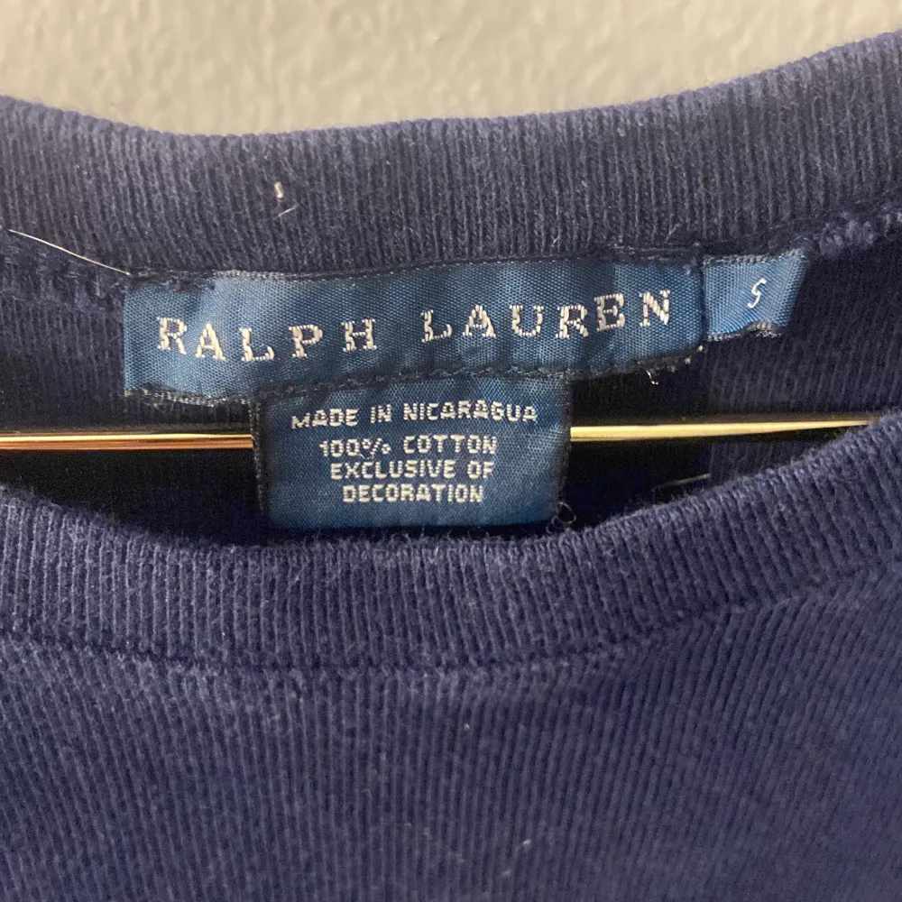 Säljer en snygg mörkblå t-shirt från Ralph Lauren i storlek S. Den är gjord av 100% bomull och har en klassisk passform med korta ärmar. Den ikoniska röda loggan är broderad på bröstet. Perfekt för en avslappnad och stilren look! (tyget är lite slitet men inget man lägger märke till, köptes på sellpy men har själv använt två gånger). T-shirts.