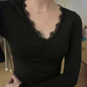 Svart långärmad topp från SHEIN - Säljer en snygg svart långärmad topp från SHEIN i storlek XS. Toppen har en vacker spetsdetalj runt den v-ringade halsen och är gjord i ett stretchigt material som ger en tight passform. Perfekt för både vardag och fest!