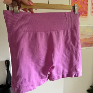 Lila tighta shorts - Säljer ett par lila tighta träningsshorts i nyskick. De är högmidjade och gjorda i ett stretchigt material som känns bekvämt mot huden. Perfekta för träning eller en avslappnad dag hemma. De har en snygg ribbad detalj vid midjan och runt benen. Aldrig använda. Storlek L