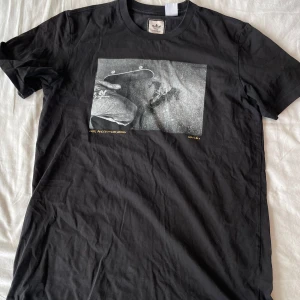 Svart t-shirt från Adidas - Säljer en svart t-shirt från Adidas med en svartvit skate-bild på framsidan. T-shirten är i storlek M och är gjord av bomull. Perfekt för vardagsbruk och under en overshirt. Den är i bra skick och väldigt bekväm att ha på sig. (ganska stor i storleken). Frågor? Skriv!