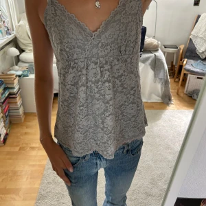 Grå spetslinne - Säljer ett superfint grått spetslinne med v-ringning och smala axelband. Det är i nyskick och väldigt bekvämt att ha på sig. Passar perfekt till jeans eller kjol!