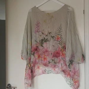 Blommig topp från Mirelle - Säljer en superfin blommig topp från Mirelle, tillverkad i Italien. Den har en lös passform och är perfekt för vår och sommar. Toppen är i en ljus beige färg med ett vackert blommönster i rosa, grönt och gult. Den har trekvartsärmar och är gjord i ett lätt och luftigt material. Linne inuti. Såg en liten maska, se foto. Därav priset.