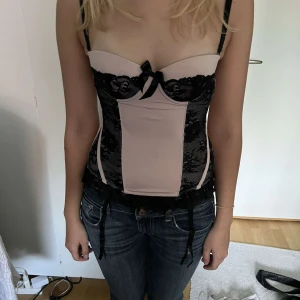 Rosa spets korsett - Rosa och svart korsett med spets och rosett detaljer. Säljes då den ej kommit till användning. Storlek och märke står ej, men skulle säga ca storlek xs/s💕