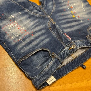 Dsquared2 Jeans storlek 50  (34) - Dsquared2 jeans är kända för sin unika stil, som kombinerar lyxig design med en edgy, street-inspirerad look. Dessa jeans är ofta präglade av en perfekt balans mellan skräddarsydd passform och en avslappnad känsla. De kan vara tillverkade av högkvalitativ denim med en viss stretch för ökad komfort och rörelsefrihet.  Vanligtvis kännetecknas Dsquared2-jeans av detaljer som distinkt slitningar, fransiga kanter eller fade-effekter, som ger ett välarbetat, “vintage” utseende, De har ofta en slim fit