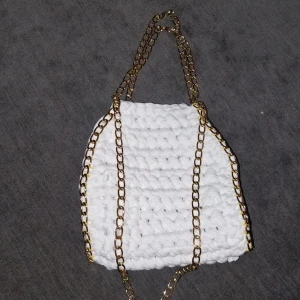 Vit virkad väska med guldkedjor - Snygg vit virkad väska med eleganta guldkedjor. Perfekt för att ge din outfit en unik touch. Väskan har en modern och trendig design som passar perfekt för olika tillfällen.