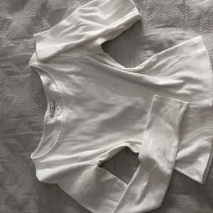 Vit ribbad långärmad topp från KappAhl - Säljer en stilren vit ribbad topp från KappAhl i storlek 170. Toppen har långa ärmar och en söt liten rosett vid halsringningen. Perfekt för en enkel och snygg look. Den är helt ny testad en gång, gick inte att returnera eftersom kvittot var borta.