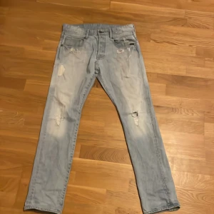 Ljusa jeans från G-Star RAW - Säljer ett par ljusa jeans från G-Star RAW med en tapered passform. De har slitna detaljer och en klassisk femficksdesign. Perfekta för en avslappnad stil.