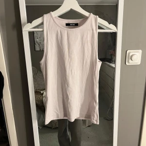 Vit linnetopp från BikBok - Säljer en stilren vit linnetopp från BikBok i storlek M. Perfekt för varma dagar med sin ärmlösa design och mjuka bomullsmaterial. Enkelt att matcha med olika outfits.