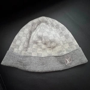 Louis Vuitton Mössa - Snygg ÄKTA grå mössa från Louis Vuitton med ett klassiskt rutigt mönster. Mössan har en uppvikt kant och är perfekt för kyligare dagar. Den är tillverkad i ett mjukt material som ger en bekväm passform.