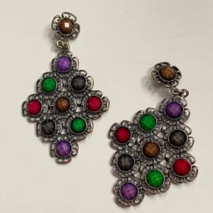 Färgglada örhängen  - Snygga örhängen med ett unikt mönster av färgglada stenar i lila, grön, röd och brun. De har en intrikat design med en silverfärgad bas som ger en elegant touch. Perfekta för att lägga till en färgklick till din outfit. Okänd metall 