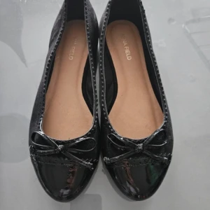 Svarta ballerinaskor med rosett - Eleganta svarta ballerinaskor från Anna Field med en glansig finish och dekorativ rosett framtill. Perfekta för en stilren look.