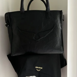 Angel tote väska Zadig & Voltaire, ny - Mycket bekväm, lagom stor och super praktisk läderväska med krinkeleffekt med handtag, axelrem och signaturstrukturerade vingar.  - Kort handtag och justerbar, avtagbar axelrem - Dragkedja - 1 platt innerficka - 1 intern ögla för att hålla en flaska - 3 inre elastiska fickor  - Ton-i-ton texturerade vingar - Kan bäras i handen, på axeln eller crossbody Mått 33 x 28 x 17 cm. Justerbar höjd på axelrem 49 till 59 cm. Vikt: 194 gram Kommer med dustbag