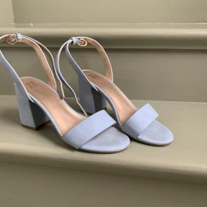 Ljusblå sandaler med klack - Snygga ljusblå sandaler med bred klack och öppen tå. De har en smal rem runt ankeln med ett spänne för justering. Perfekta för en stilren look.