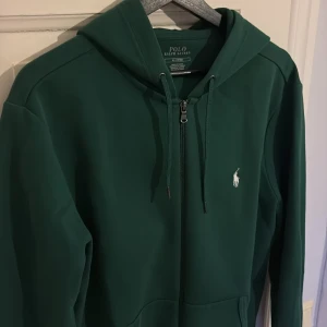 Grön hoodie från Ralph Lauren - Säljer en snygg grön hoodie från Ralph Lauren med dragkedja. Den är knappt använd och i utmärkt skick. Köpt på NK Göteborg för 1,8k. Skriv vid funderingar!