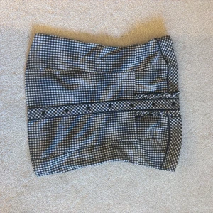 Rutig topp från Mohito - Snygg rutig topp från Mohito i svart och vit med volangdetaljer och knappar framtill. Perfekt för en stilren look. Tröjan har en bra längd och är gjord i ett bekvämt material. Dragkedja på sidan. Säljer pågrund av flytt och för mycket kläder 😆😆