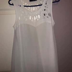 Vit ärmlös klänning från Sisters Point - Snygg vit ärmlös klänning från Sisters Point med ett unikt utskuret mönster vid halsringningen. Perfekt för sommarens varma dagar. Klänningen har en luftig passform och är gjord i ett lätt material.