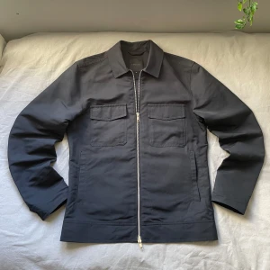 Marinblå jacka från Elvine - Snygg svart jacka från Elvine med dragkedja framtill och två praktiska bröstfickor. Jackan har en klassisk krage och är perfekt för en stilren look. Passar bra till både vardag och mer uppklädda tillfällen. Jackan är gjord i 62% nylon och 38% polyester så den har en lite mer regntät känsla  Bara att höra av sig om man har några frågor🤗