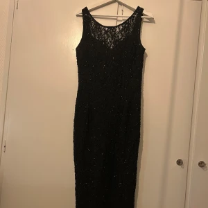 Svart spetsklänning med slits - Elegant svart långklänning i spets med glittrande detaljer i form av pärlor. Klänningen har en slits baktill och djup rygg som ger en sofistikerad touch. Lånade bilder bild 4 & 5. Skriv om du vill ha mer info eller fler bilder ✨