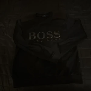 Svart tröja från Hugo Boss - Säljer en stilren svart tröja från Hugo Boss med stort BOSS-tryck på framsidan. Tröjan har en slim fit passform och långa ärmar, perfekt för en snygg och bekväm look.