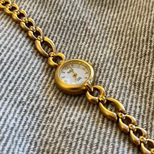 Liten vintage klocka - Liten vintage klocka i guldfärg. Metallen på själva uret är i rostfritt stål, även metallen på klockan är det. Den är också water resistant. Vet inte om klockan är guldpläterad, men den har inte tappat någon guldfärg trots att modellen är mycket gammal. Batteriet i uret har tyvärr slutat funka, men går säkert att byta ut om man vill att den ska funka igen! Omkretsen är 18,5 cm. Aldrig använd då plasten på baksidan av uret fortfarande är kvar!