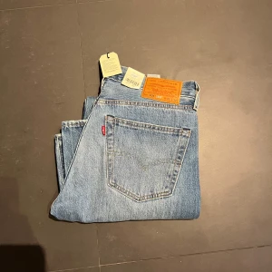Helt nya Blå Levis 501 jeans - Säljer ett par klassiska blå Levis 501 jeans. De har en straight passform och är tillverkade i 100% bomull. Jeansen har slitna detaljer på framsidan för en trendig look. Perfekta för en avslappnad stil. Nypriss 1349 mitt endast 500.