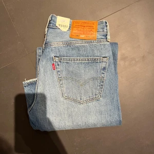 Helt nya Levi's 501 jeans i ljusblå denim - Klassiska Levi's 501 jeans i ljusblå denim med en straight passform. De har en vintage look med slitningar på framsidan och den ikoniska läderpatchen bak. Perfekta för en avslappnad stil.