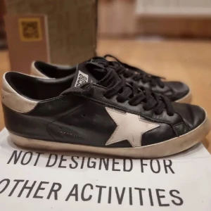 Svarta sneakers med vit stjärna - Snygga svarta sneakers med en vit stjärna på sidan. Skorna har snörning och en klassisk design som passar perfekt för en avslappnad stil. De är tillverkade i skinn och har en robust sula för extra komfort.