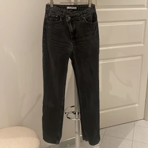 Jeans  - Ett par grå/svarta jeans som är raka i modellen och har en sned midjedetalj. 