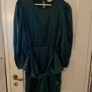 Mörk grön satin klänning  - En fin mörkgrön satin klänning, med trekvarts armar. Använd 1 gång och har inga fläckar eller några hål, nypriset ligger runt 600kr.