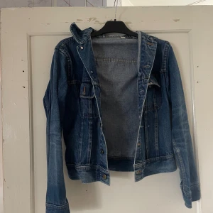 Blå jeansjacka från Jeans Center - Säljer en klassisk blå jeansjacka från Jeans Center. Den har en snygg och tidlös design med knappar framtill och två bröstfickor. Perfekt för vår och sommar! Jackan är i storlek 36 och passar perfekt för en casual look.
