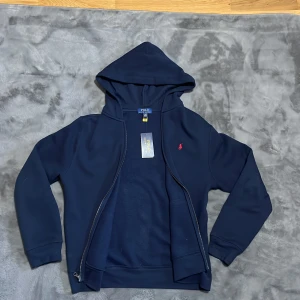Mörkblå hoodie från Polo Ralph Lauren - Säljer en snygg mörkblå hoodie från Polo Ralph Lauren.Aldrig använd bara testad!! Perfekt för höst och vinter, och den är i nyskick med etiketten kvar. Superbekväm och stilren, perfekt för både vardag och chill!! Storlek 170/S