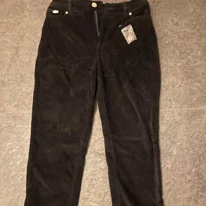 Svarta manchesterbyxor - Snygga svarta manchesterbyxor med klassisk design. Byxorna har en rak passform och är perfekta för både vardag och mer uppklädda tillfällen. De har knappar och dragkedja framtill samt fickor både fram och bak.