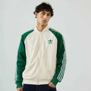 Vit och grön jacka från Adidas - Snygg vit och grön jacka från Adidas med klassiska tre ränder på ärmarna. Jackan har dragkedja och Adidas-logga på bröstet. Aldrig använd med prislappar kvar! Köpt för 800 kr. 
