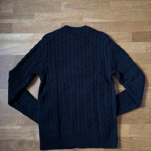 Svart kabelstickad tröja från Selected Homme - Säljer en stilren svart kabelstickad tröja från Selected Homme. Tröjan har en klassisk design med ribbade muddar vid ärmslut och nederkant. Perfekt för kyliga dagar|oanvänd|storlek S|100% bomull|