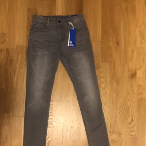 Grå skinny jeans från Blue Ridge - Snygga grå skinny jeans från Blue Ridge i storlek 158. De har en klassisk femficksdesign och är perfekta för en stilren look. Jeansen har en knappgylf och bälteshällor för extra stilpoäng.