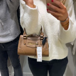 Beige handväska från Gina - Snygg beige handväska från Gina med dekorativa sömmar och helt oanvänd Väskan har dubbla handtag och en avtagbar axelrem för extra bekvämlighet.