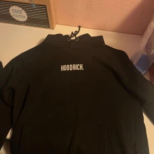 Svart hoodie från Hoodrich - Säljer en svart hoodie från Hoodrich med tryck på bröstet. Den har en klassisk design med dragsko i huvan och en stor magficka. Perfekt för en avslappnad stil.