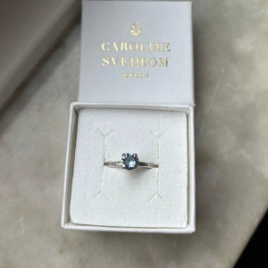 Caroline Svedbom Natti ring i utmärkt skick - Natti Ring från Caroline Svedbom i Light Sapphire färgen, perfekt som julklapp. Sparsamt använd, i jättebra skick, har pytteliten missfärgning på baksidan av ringen, syns ej (bild 5). Rodium plätering, öppen baksida och justerbar storlek. Priset kan diskuteras vid snabb affär. Slutsåld, nypris 395 kr. Säljer flera smycken från Caroline Svedbom